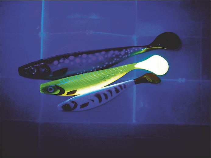 Ein UV-aktiver Köder leuchtet im Dunkeln neben zwei nicht-UV-aktiven Ködern.