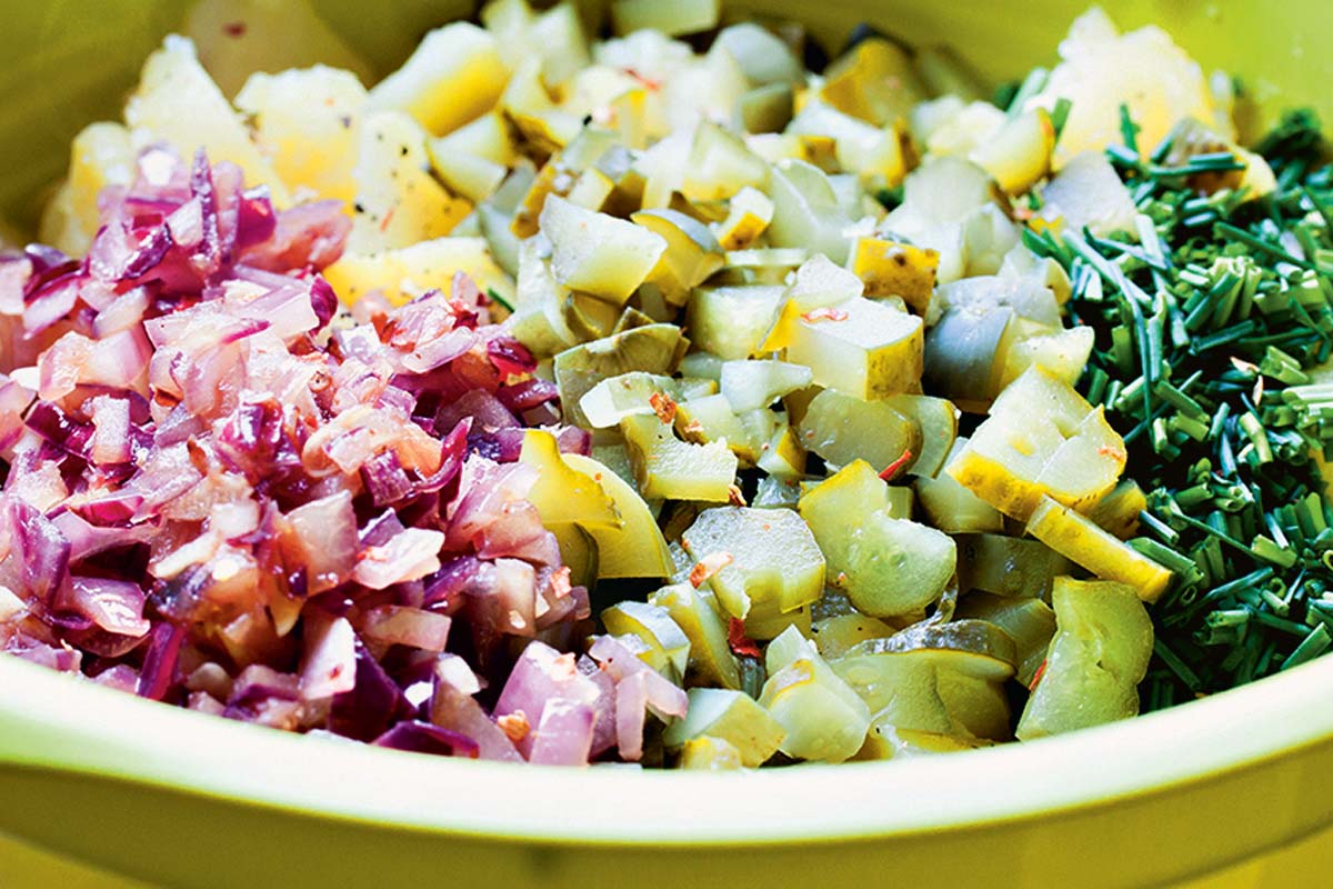 Die (vorgekochten) Kartoffeln und die sauren Gurken in Stücke schneiden. Zwiebeln und Knoblauch würfeln und glasig anbraten. Anschließend mit 500 ml Brühe, Essig und gehacktem Schnittlauch in einer Schale vermischen. Mit Chili, Salz und Pfeffer abschmecken und eine Stunde in den Kühlschrank stellen, damit der Salat gut durchziehen kann. Foto: Artur Jagiello