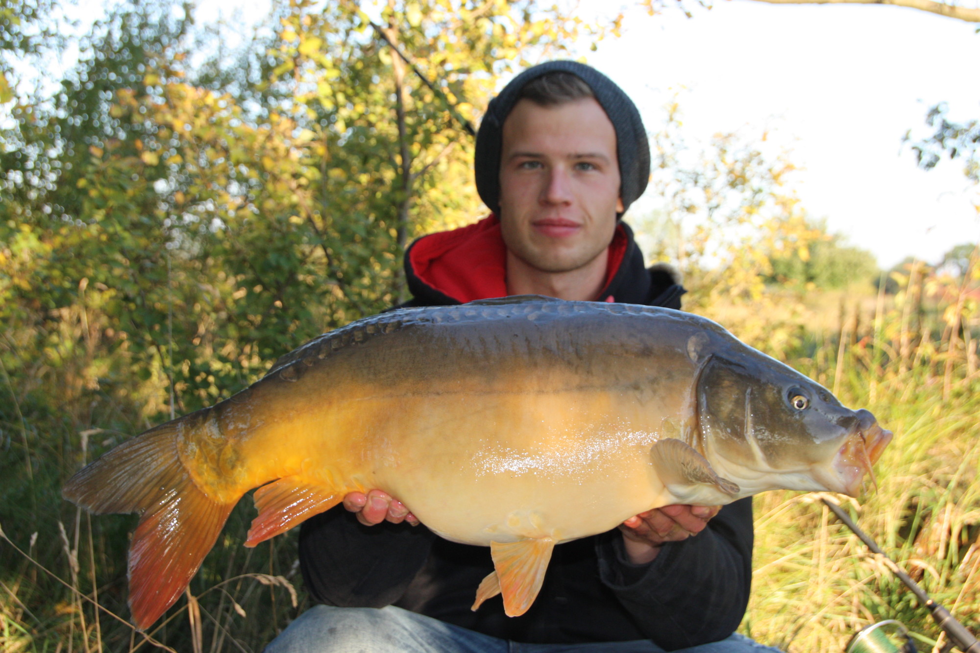 Der Autor hält einen großen Karpfen auf dem Arm. Im Hintergrund ist der See im Frühling zu sehen.