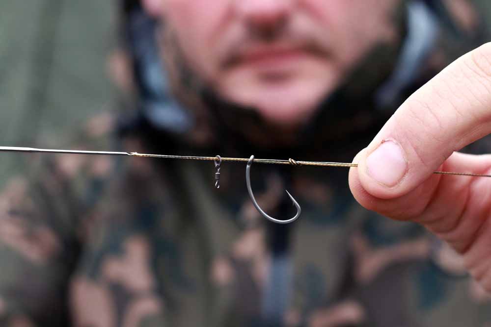 Unter Zuhilfenahme einer Ködernadel wird die Schlaufe von innen nach außen durch das Öhr des Curve-Hakens gezogen. Anschließend schiebt man den Micro-Ring-Swivel auf die Schlaufe. 