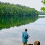 Ein Angler steht am Rande eines Sees im Wald und angelt.
