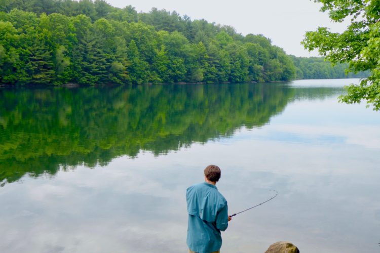 Ein Angler steht am Rande eines Sees im Wald und angelt.