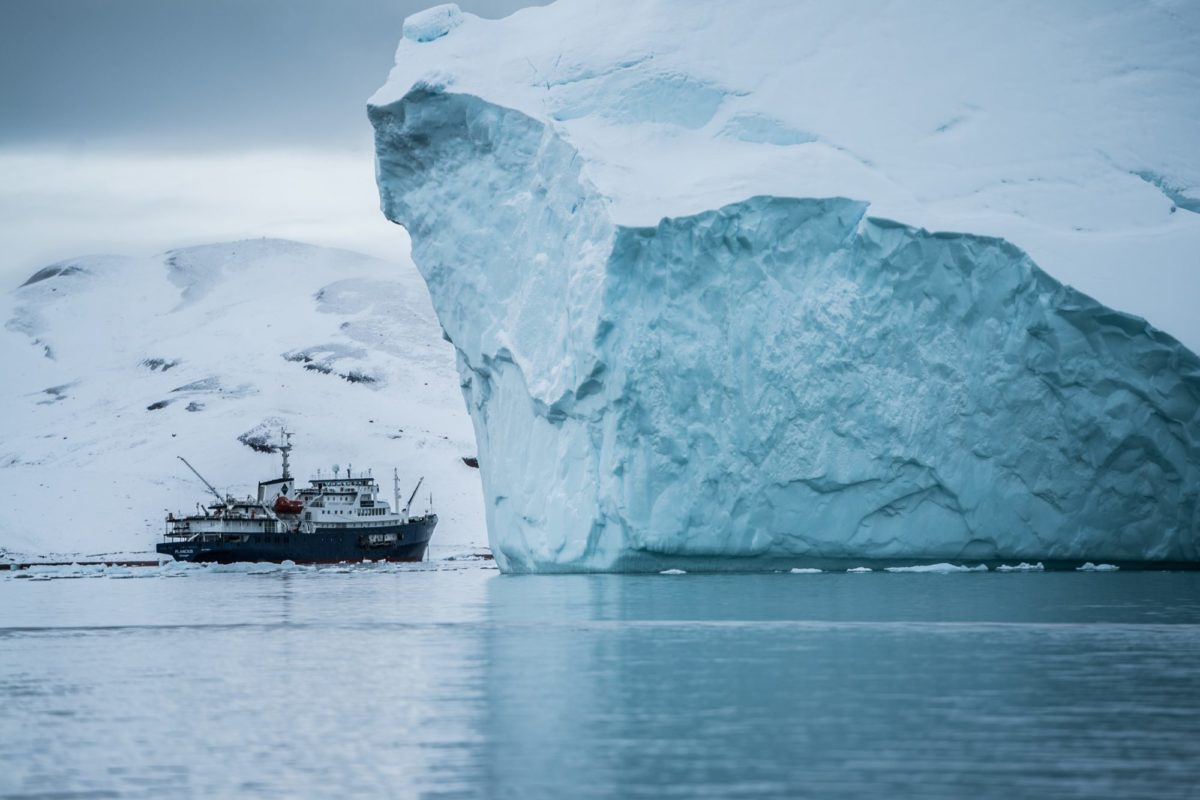 Auf dem Wasser fährt ein kleines Schiff hinter einen großen Eisberg.
