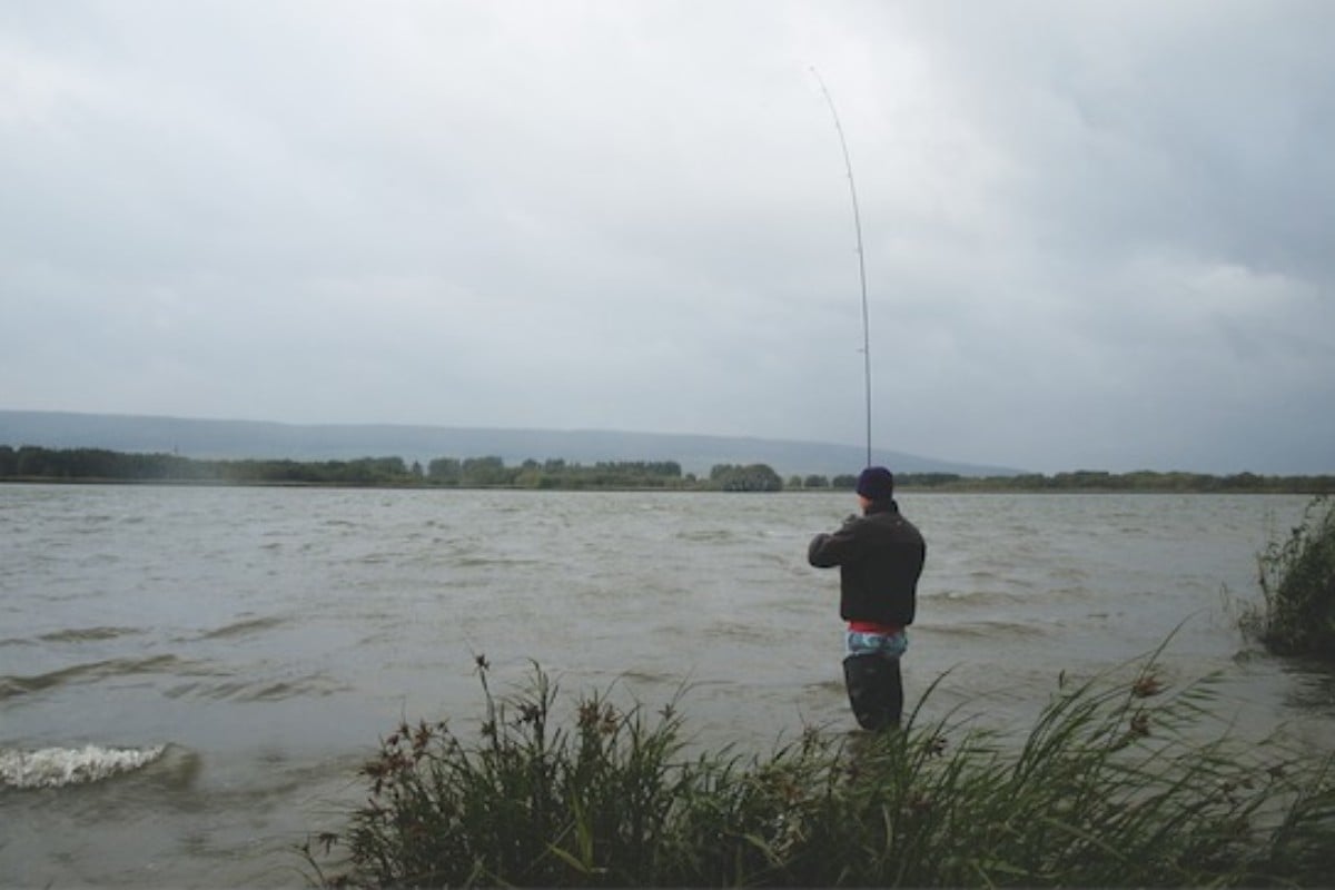 Angler steht im seichten Wasser in schlechten Wetter und angelt.