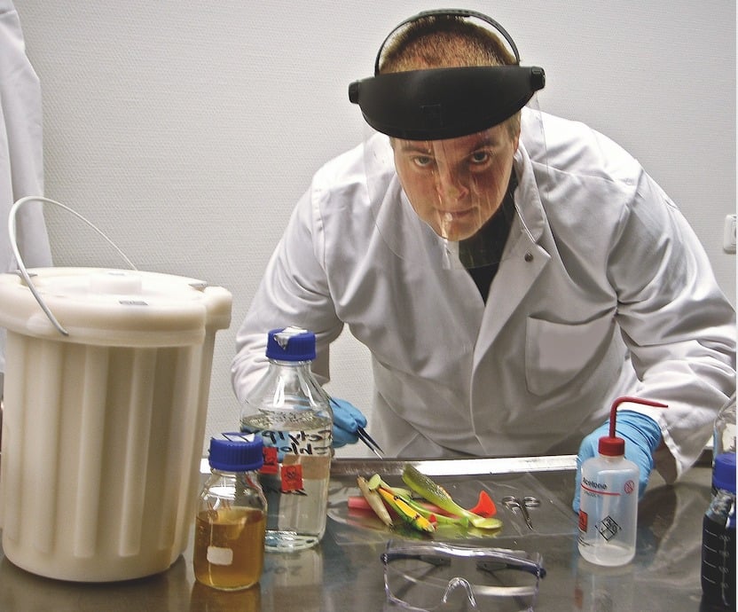 Ein Mann mit Laborkittel und Gesichtsschutz steht vor einem Labortisch.
