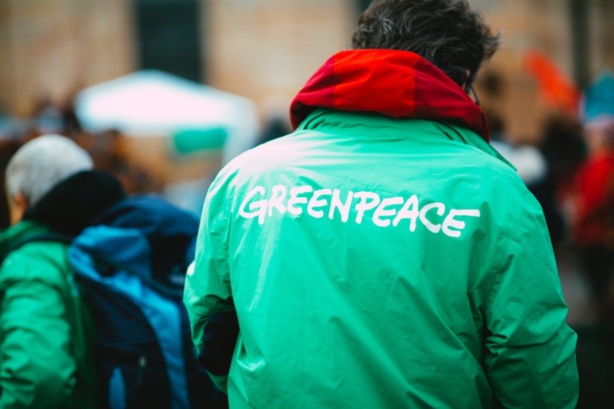 Mann steht mir dem Rücken zur Kamera. Er trägt eine grüne Jacke auf der in weißer Schrift "Greenpeace" steht.