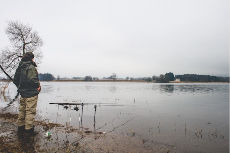 Angler beim winterlichen Hechtansitz an einem Baggersee. Zwei Köder sind auf größere Entfernung ausgelegt, einer dritter jedoch in Ufernähe.