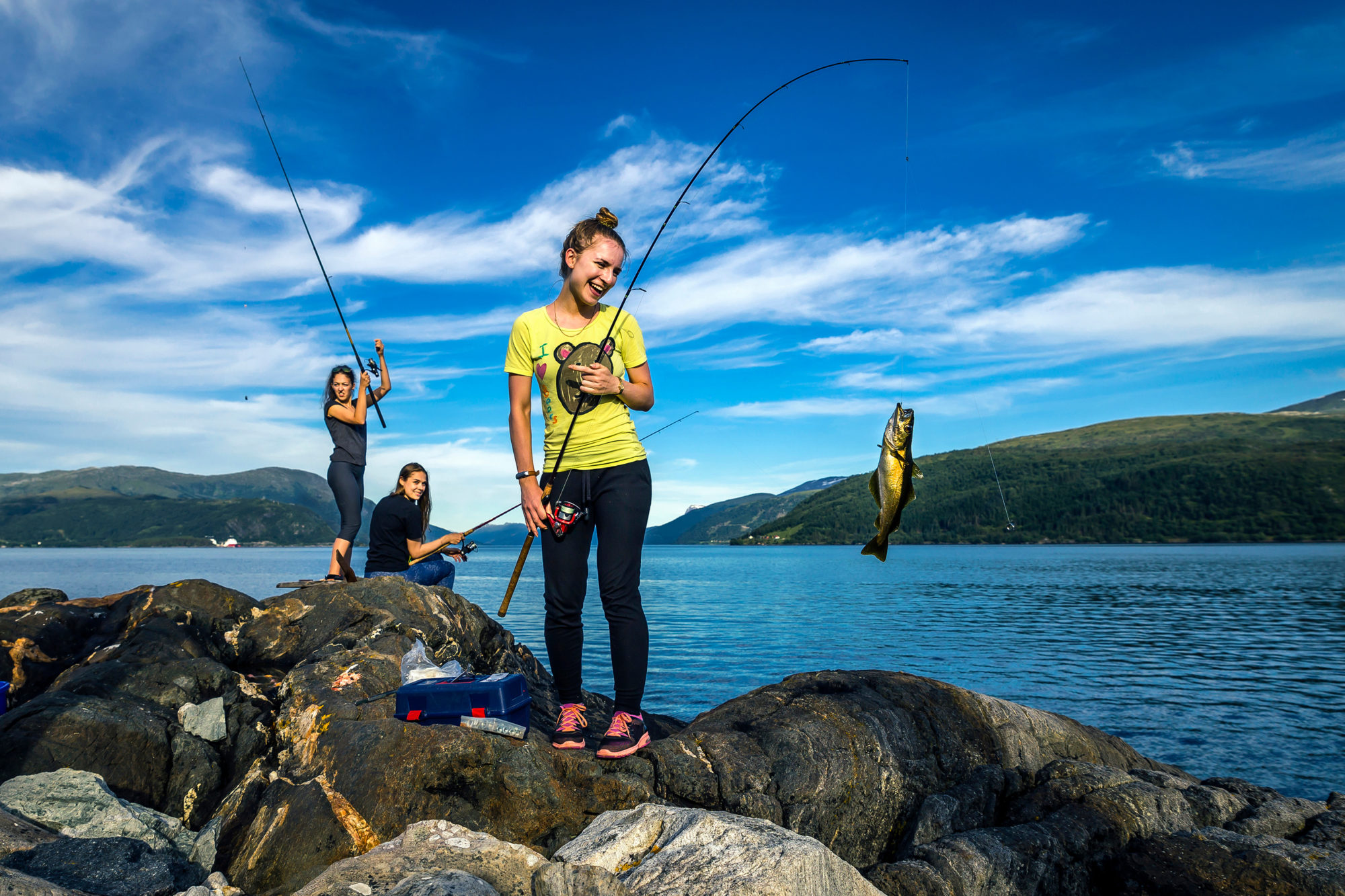 Young people are fishing on the rocks next to the fjord, Norway
