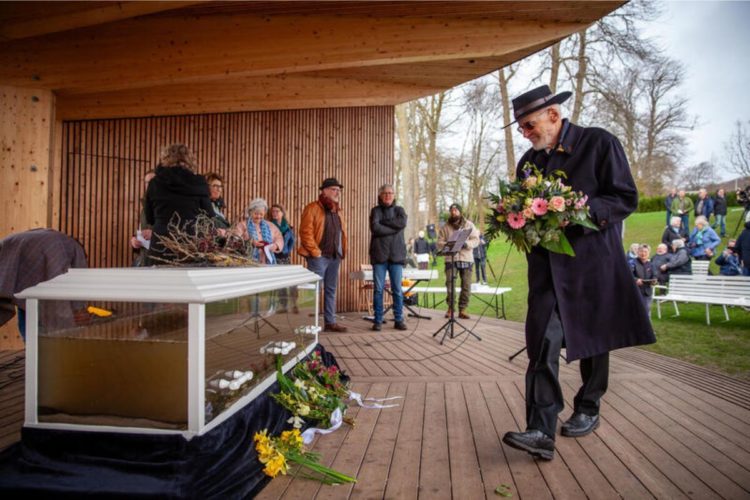 Mann legt Blumenstrauß an Sarg voller Wasser nieder