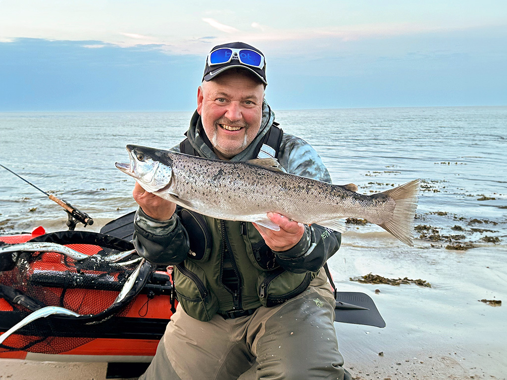 Angler mit Meerforelle am Ostseestrand, im Hintergrund ein Bellyboot