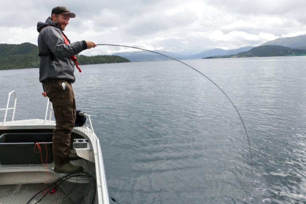 Angler mit krummer Fliegenrute auf einem Boot im Fjord