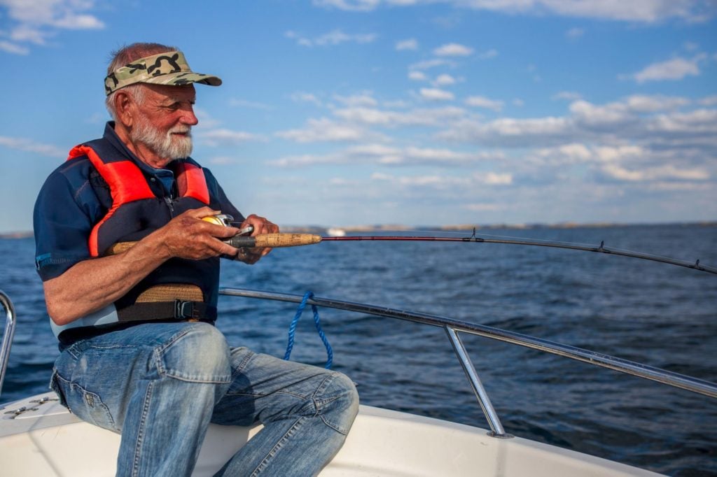 Alter Angler drillt einen Fisch vom Boot, die Sonne scheint