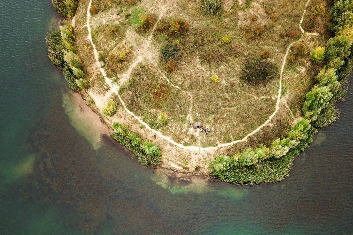 Luftbild der Uferkante eines Gewässers mit Angler in einem Zelt am Ufer