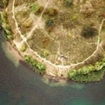 Luftbild der Uferkante eines Gewässers mit Angler in einem Zelt am Ufer