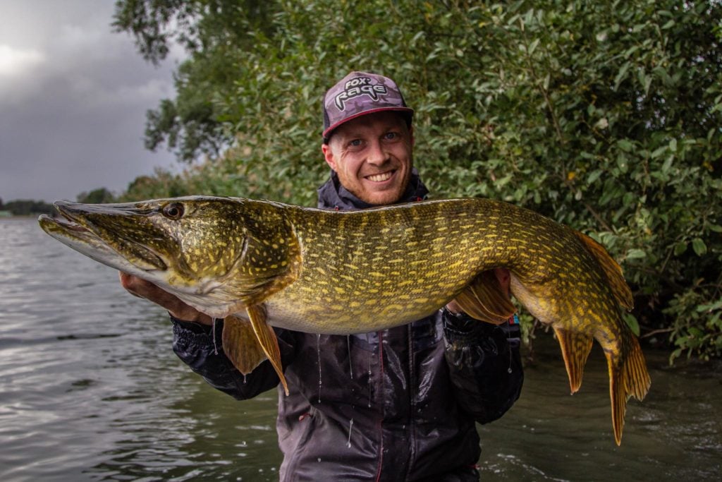 Angler mit großem Hecht, im Hintergrund regnet es