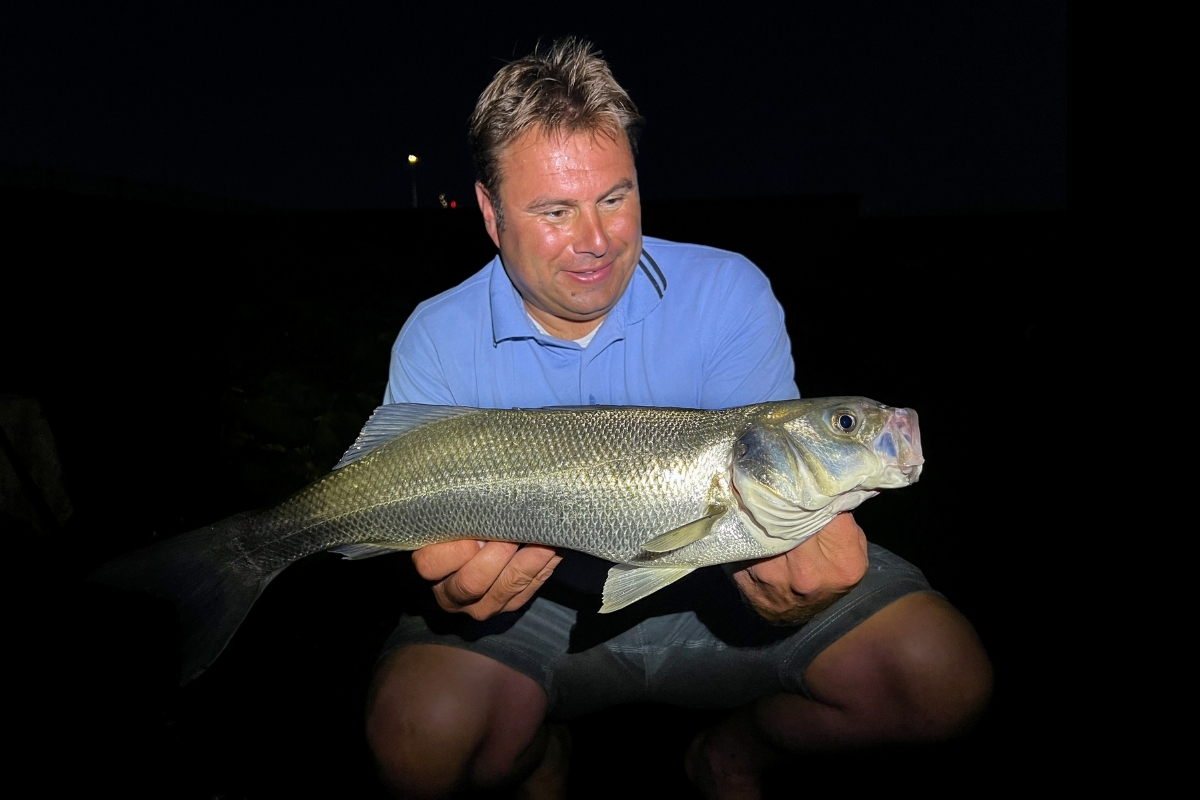 Angler mit Wolfsbarsch in der Nacht