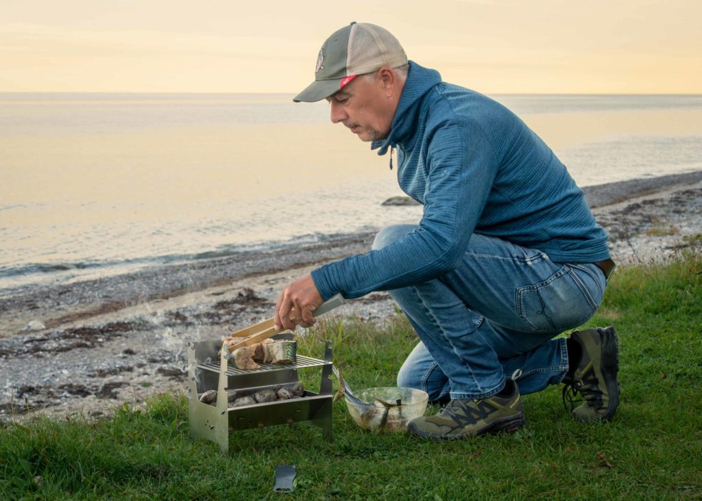 Mann grillt Makrelen am Strand