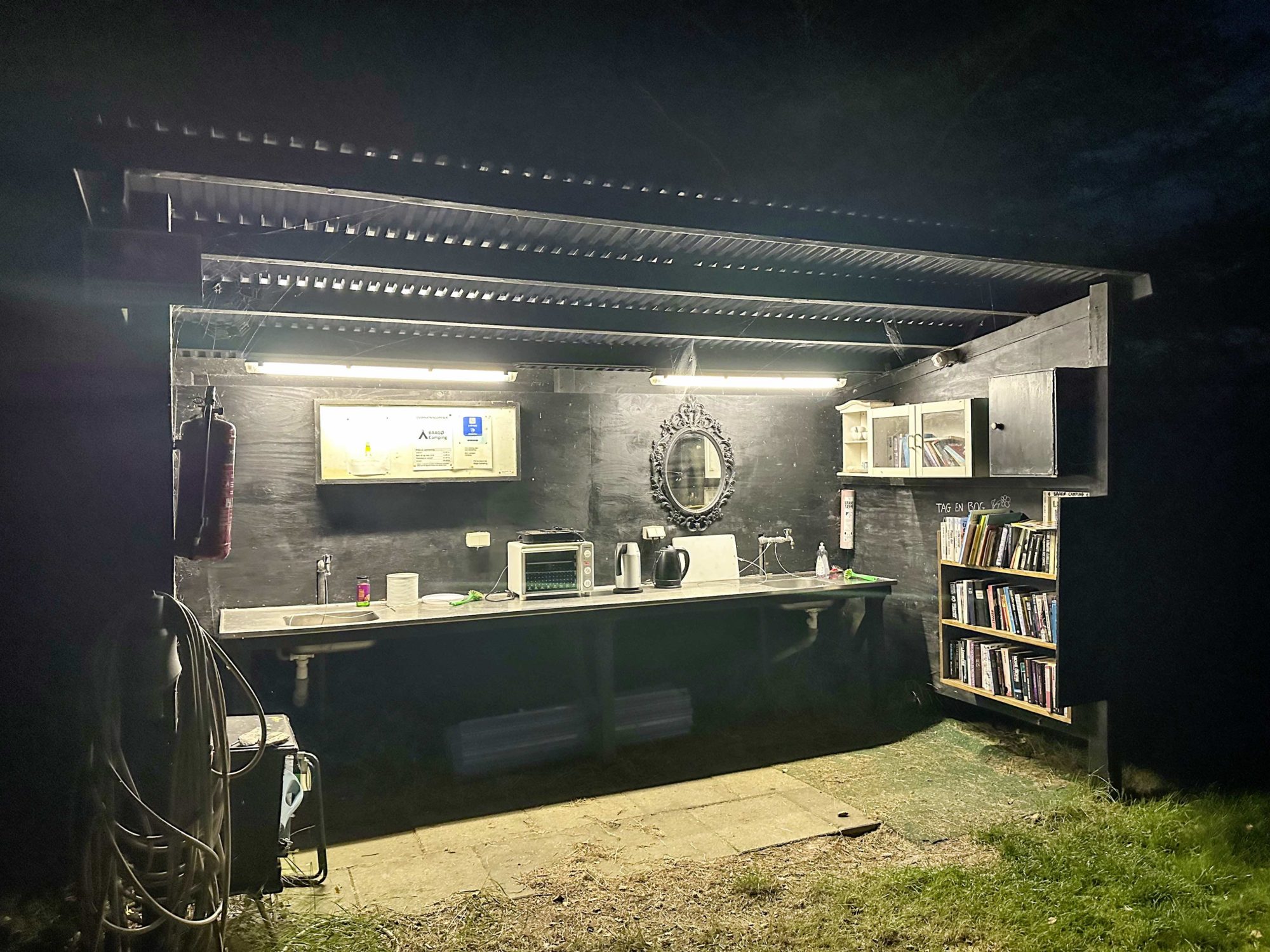 Service auf dem Campingplatz: eine überdachte Küche mit Waschbecken, Mikrowelle, Toaster, Wasserkochern und Büchern zum Ausleihen.