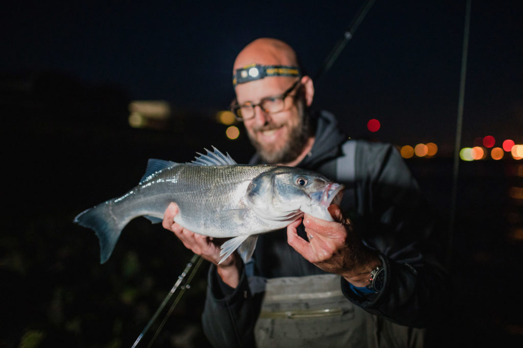 Angler mit Wolfsbarsch in der Nacht