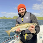 Angler mit Pollack auf Boot, er trägt eine Schwimmweste