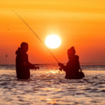 Zwei Angler beim Angelurlaub in Dänemark angeln an der Küste im Sonnenaufgang