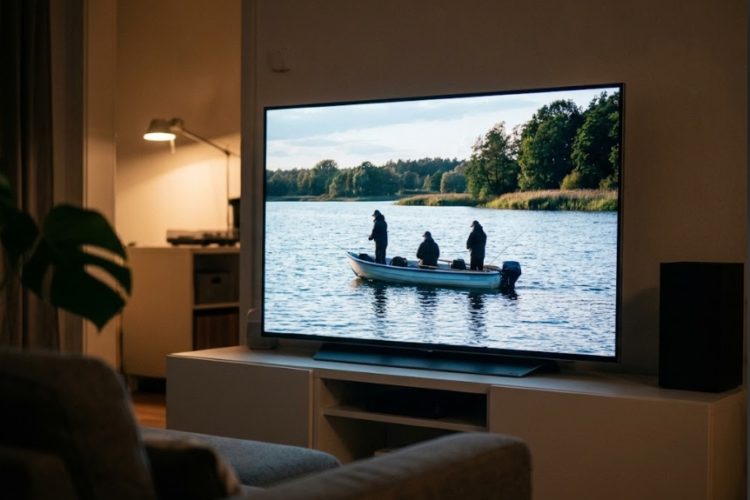 Ein Fernseher im Wohnzimmer zeigt eine Angelsendung mit drei Anglern in einem Boot auf einem See.